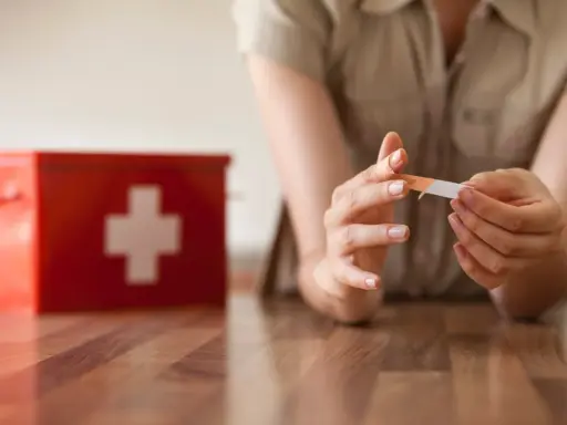 Une personne applique un pansement sur son doigt, près d'une trousse de secours rouge. L'objectif est une cicatrisation rapide.