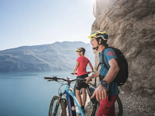 Ein Paar genießt die Aussicht auf den Gardasee während einer E-Bike-Tour. Die Berge und das klare Wasser bilden eine atemberaubende Kulisse.
