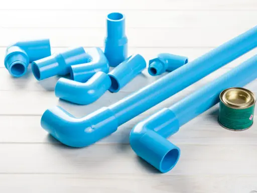 Ensemble de tuyaux et raccords bleus en PVC, prêts pour une installation. Un pot de colle est à proximité.