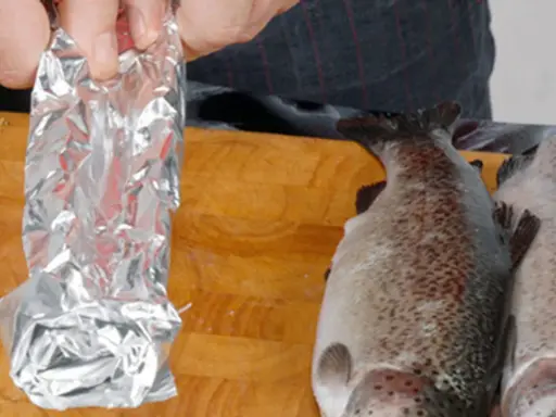 Vorbereitung für das Grillen: Ein Fisch wird in Alufolie gewickelt, bereit für den Weber Grill.