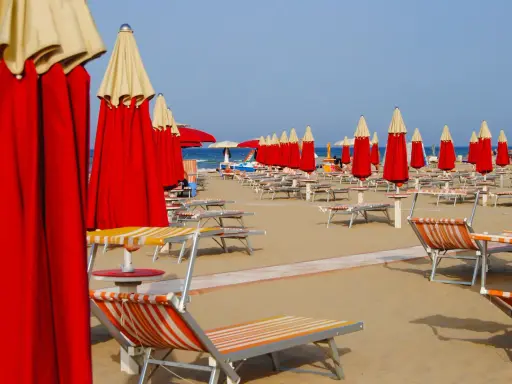 Filetto di ombrelloni rossi e lettini pronti per accogliere i bagnanti sulla costa di Rimini.