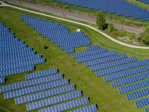 Große Solaranlage auf einer grünen Wiese mit Gleisen im Hintergrund.