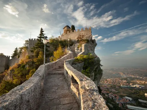 Sentiero in pietra che sale verso le fortificazioni di San Marino città, con vista panoramica sulla valle sottostante.