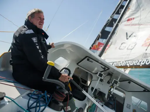 Un homme expérimenté, kito de pavant, tient la barre d'un voilier, concentré sur la course.