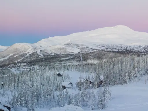 Snötäckta berg och skog med små stugor, en idyllisk vy över mindre skidorter Sverige i skymningen.