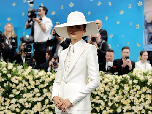 Zendaya, deslumbrante con traje blanco y sombrero, posa ante cámaras y flores.