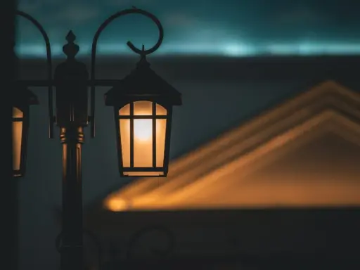 Ciepłe światło zabytkowych lamp miejskich rozświetla zmierzch, rzucając geometryczne cienie na budynek.