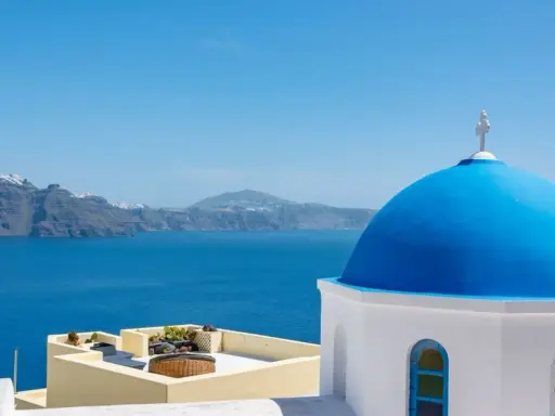 Blaue Kuppel einer Kirche in Oia, Santorini, mit Blick auf das tiefblaue Meer und die zerklüftete Küste.
