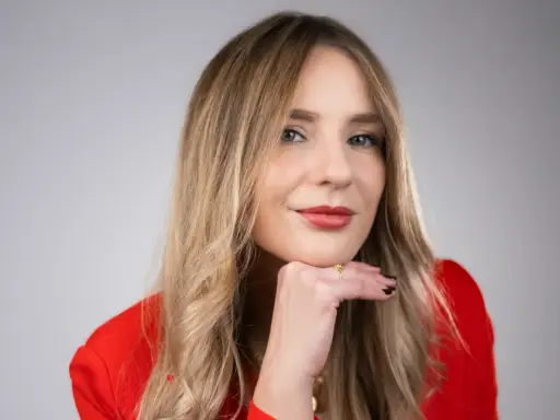 Francesca Florio, con un blazer rosso, appoggia il mento sulla mano, un sorriso pensieroso.