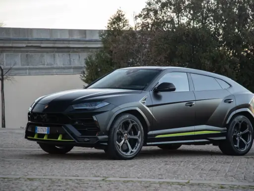 Un imponente **lamborghini urus negro** se exhibe con detalles en verde lima, posado sobre un camino empedrado.
