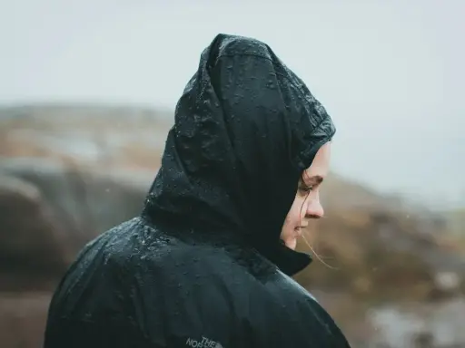 Person i regnkläder med huvan uppdragen, droppar på tyget. Vattenpelare 10000 klarar detta väder.