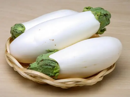 Trois aubergines blanches, d'une blancheur immaculée, reposent dans un panier en osier tressé sur un fond en bois clair.