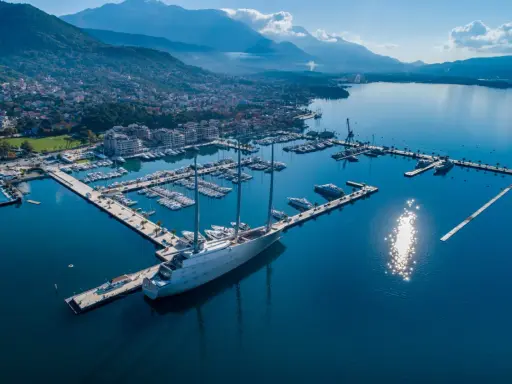Ein riesiges Segelschiff liegt im porto hafen, umgeben von vielen Yachten und einer Stadt am Fuße von Bergen.