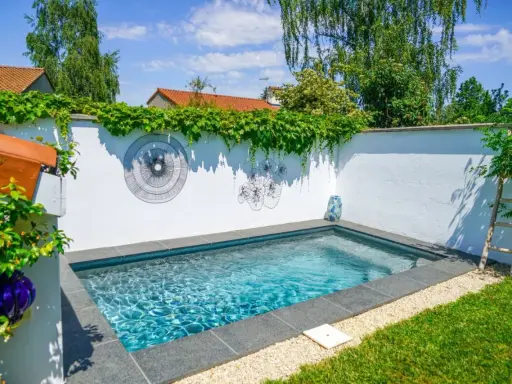 Petite piscine bleue dans un jardin verdoyant, décorée d'art mural. Un projet de permis de construire piscine réussi.