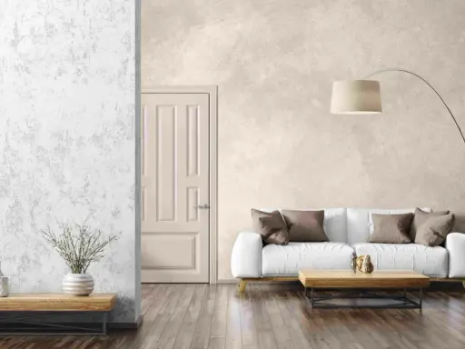 Un salon moderne avec un mur texturé en enduit décoratif, un canapé blanc, une table basse en bois et une plante verte.