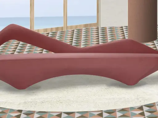 A pink velvet sofa with a unique curved design sits on a cream rug in a room with a geometric tiled floor and a view of the ocean.