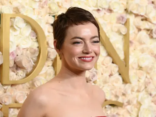 Emma Stone sorride, con un trucco che esalta i colori che stanno bene alle castane con pelle chiara. Lo sfondo è un muro di rose rosa e bianche.