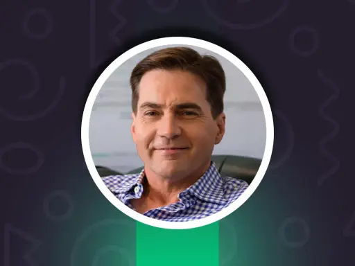 Uśmiechnięty Craig Wright w niebiesko-białej koszuli w kratę, z kluczem w lewym górnym rogu.