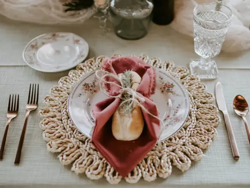 Une table dressée avec élégance, une assiette fleurie, une serviette bordeaux et une **fourchette à la française** en cuivre, prête pour un repas raffiné.