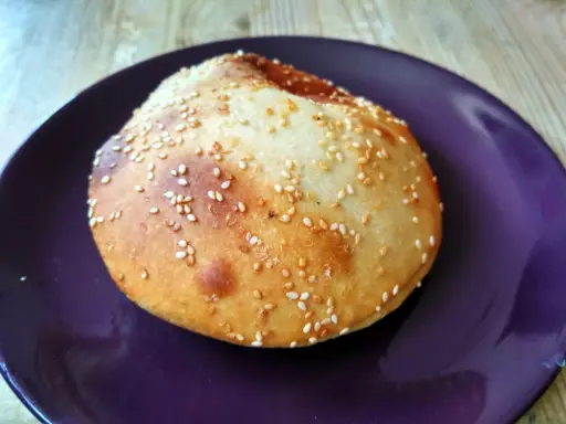 Bułka do hamburgerów posypana sezamem na fioletowym talerzu.