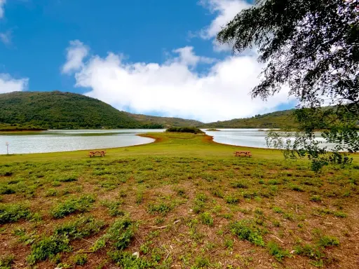 Prato verde con tavoli da picnic affacciati sul **lago di Canterno**, circondato da dolci colline sotto un cielo azzurro con nuvole bianche.