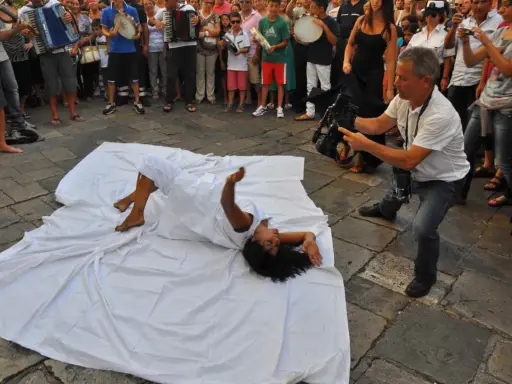 Danza contemporanea durante la festa patronale Galatina. Un performer si muove su un telo bianco, ripreso da un operatore.