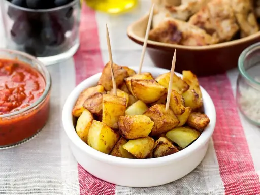 Patatas bravas dorées, servies avec une sauce tomate épicée et des olives. Un délice pour l'apéro !