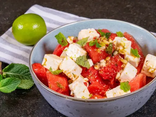 Erfrischender Wassermelonen-Feta-Salat mit Minze und Pinienkernen, garniert mit Limettenabrieb. Perfekt für heiße Tage.