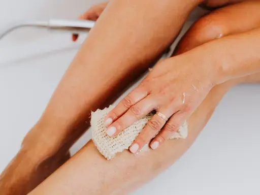 Une main utilise un gant de toilette pour exfolier sa peau, révélant une peau douce et lisse. C'est une étape clé pour savoir comment exfolier sa peau.
