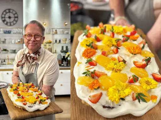 En glad man håller upp en vacker påsktårta i långpanna, dekorerad med grädde, jordgubbar, aprikoser och gula blommor.