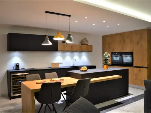 Une cuisine moderne aux accents beige et noir, avec un îlot central, des meubles en bois et des suspensions colorées.