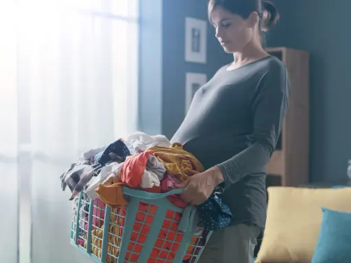Ciężarna kobieta z koszem prania. Dźwiganie w ciąży bywa wyzwaniem, ale ona radzi sobie z codziennymi obowiązkami.