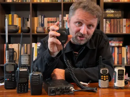 Mężczyzna prezentuje sprzęt CB radio, pokazując różne modele i akcesoria, które wpływają na zasięg.