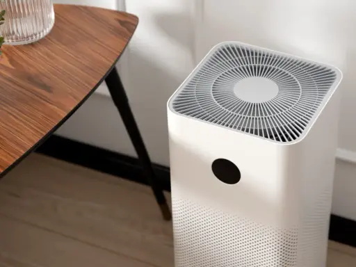 Purificador de aire blanco junto a una mesa de madera. Muestra cómo funciona un purificador de aire al aspirar y limpiar el aire.