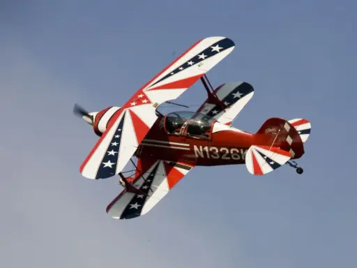 Rotes Pitts Special Doppeldeckerflugzeug mit Sternenmuster fliegt im blauen Himmel.
