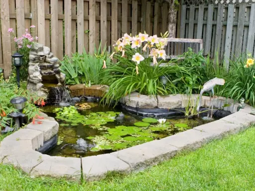 Un estanque en el jardín con cascada, lirios y decoración de grulla. Ideal para aprender como hacer un estanque en el jardin.