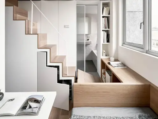 Monolocale con soppalco: scala in legno e bianco, bagno con doccia, scrivania e letto integrati.