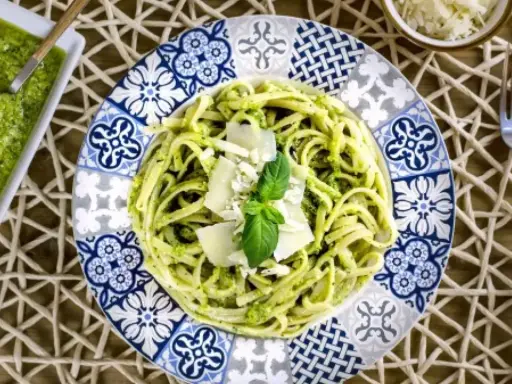 Deliciosa pasta con pesto, ideal para tus recetas de pasta con pesto. Servida en un plato decorado con un toque mediterráneo.