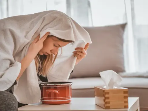 Une femme apprend comment faire une inhalation, la tête couverte d'une serviette au-dessus d'une casserole de vapeur.
