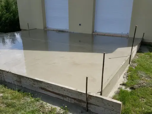 Une nouvelle dalle béton fraîchement coulée, prête à sécher. Les coffrages en bois et les fers à béton délimitent la zone.