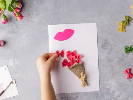 Manos creando flores manualidades con pasta de moño rosa, un ramo y labios de papel.