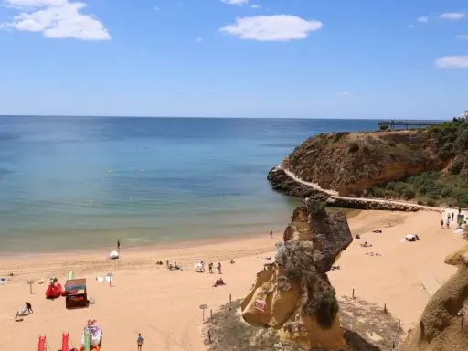 Sonniger Lagos Strand mit goldenem Sand, türkisfarbenem Wasser und Felsformationen. Menschen entspannen sich, spielen und genießen die Aussicht.
