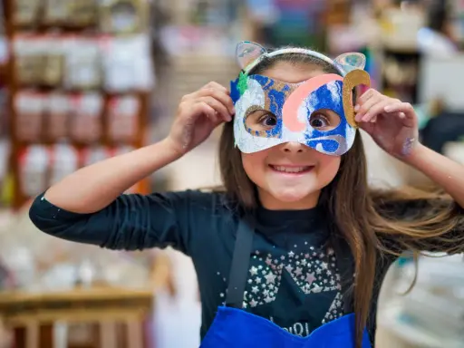 Une jeune fille, le visage caché par un masque coloré, explore la symbolique du visage et la joie de la transformation.