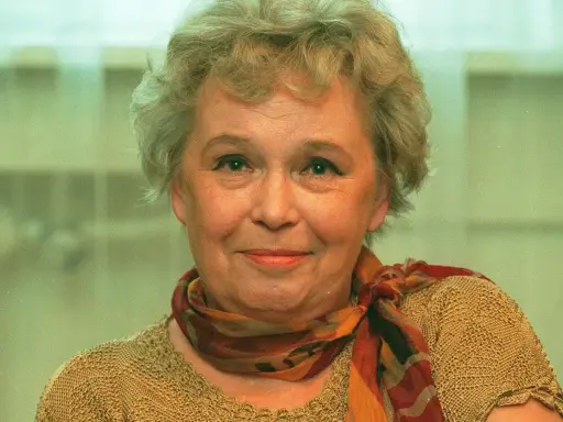 Uśmiechnięta Joanna Chmielewska, autorka kultowych powieści kryminalnych, w beżowym swetrze i kolorowym szalu.