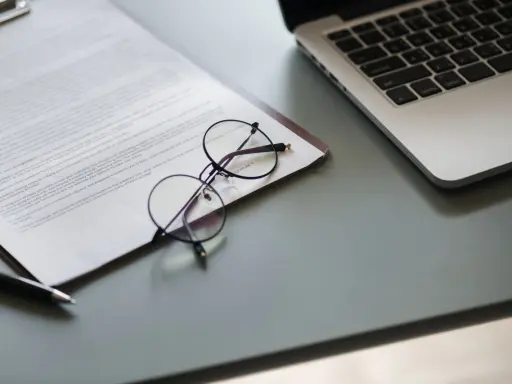 Okulary na dokumencie z tekstem, obok laptopa. Dokument może zawierać pełnomocnictwo lub strategię marketingową.