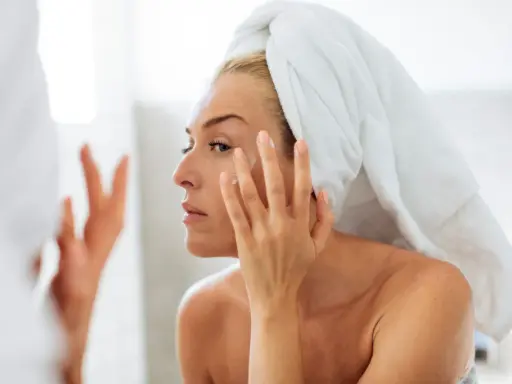 Une femme, serviette sur la tête, applique une crème sur son visage. Un geste essentiel pour prendre soin de sa peau en hiver.
