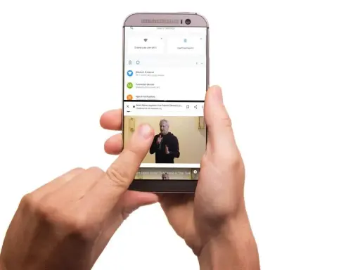 Dwie ręce trzymają telefon, na którym widać, jak podzielić ekran na 2. Górna część pokazuje ustawienia, dolna odtwarza wideo.