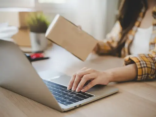Osoba pakuje paczkę, sprawdzając na laptopie, kto ponosi koszty zwrotu towaru.