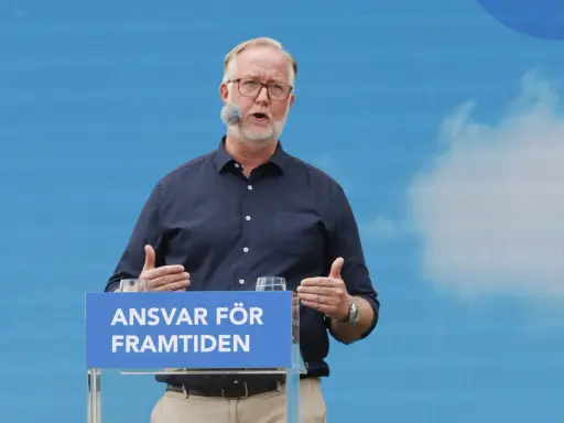 Man med glasögon och mikrofon talar vid ett podium med texten "Ansvar för framtiden". Hans gestik och budskap speglar en liberalism ideologi.