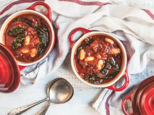 Due ciotole rosse con zuppa di cavolo nero, fagioli e pomodoro, pronte per essere gustate.